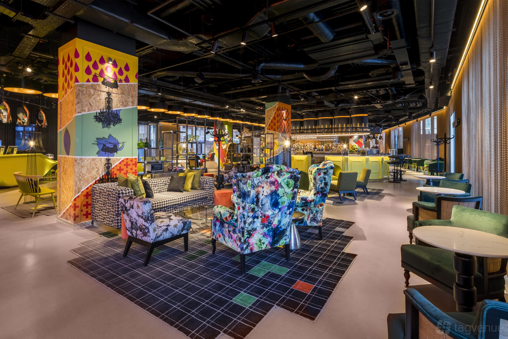 An open-plan hotel event space with colorful patterned armchairs, lounge seating, and vibrant pillar art at nhow London.