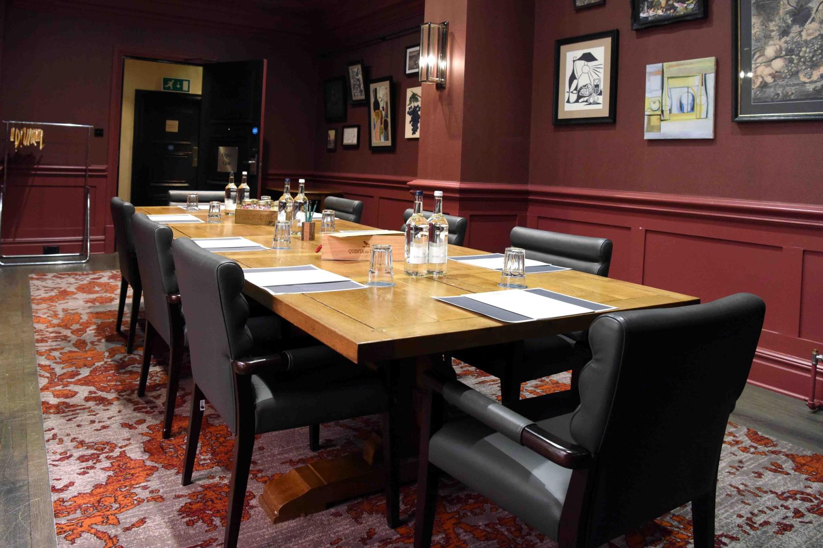 A hotel meeting room with a long wooden table, black chairs, bottled water, and framed artwork at Hotel du Vin Birmingham.