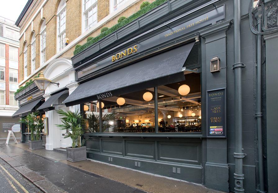 A versatile event space with large street-facing windows, globe pendant lights, and black awnings at Bonds