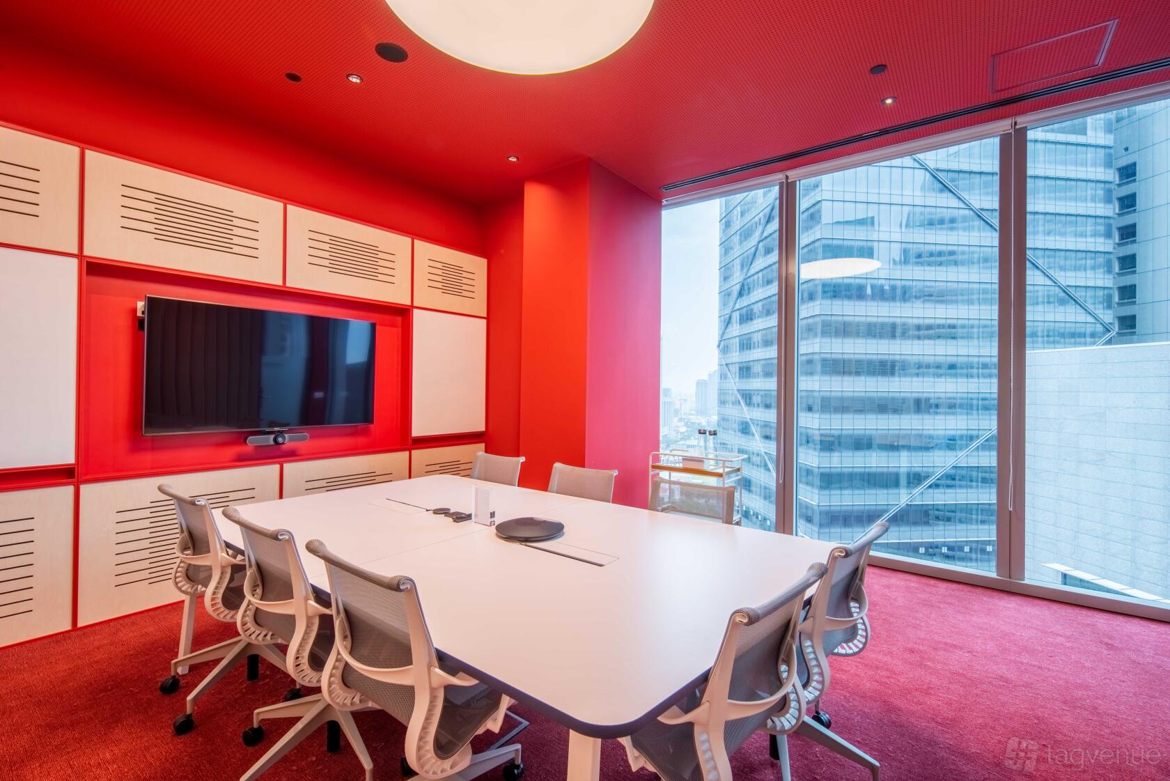 A boardroom with a large white table, ergonomic chairs, wall-mounted screen, and floor-to-ceiling windows at The Work Project CapitaSpring.