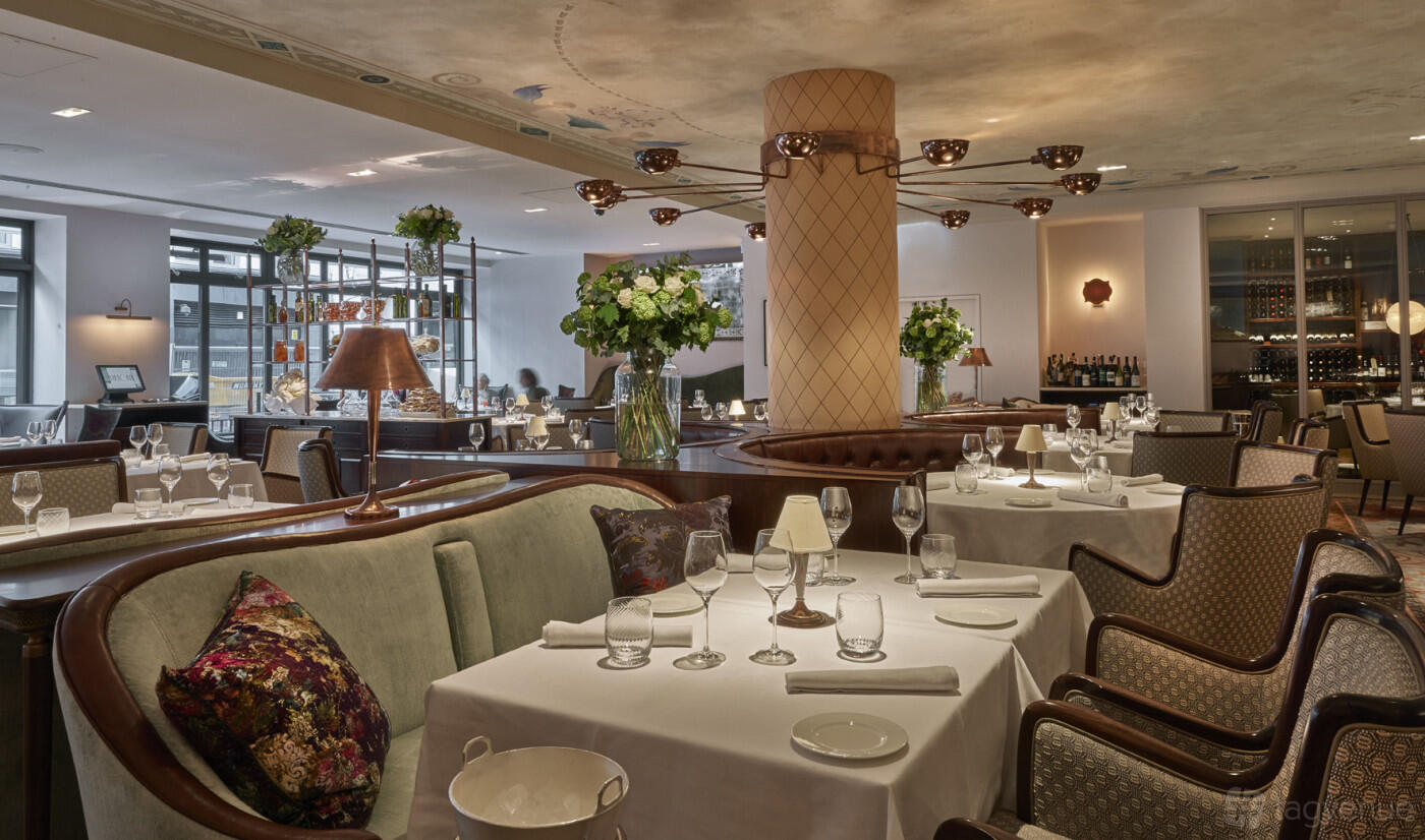 A restaurant dining room with round tables set with glassware, plush banquettes, and floral centerpieces at Sartoria.