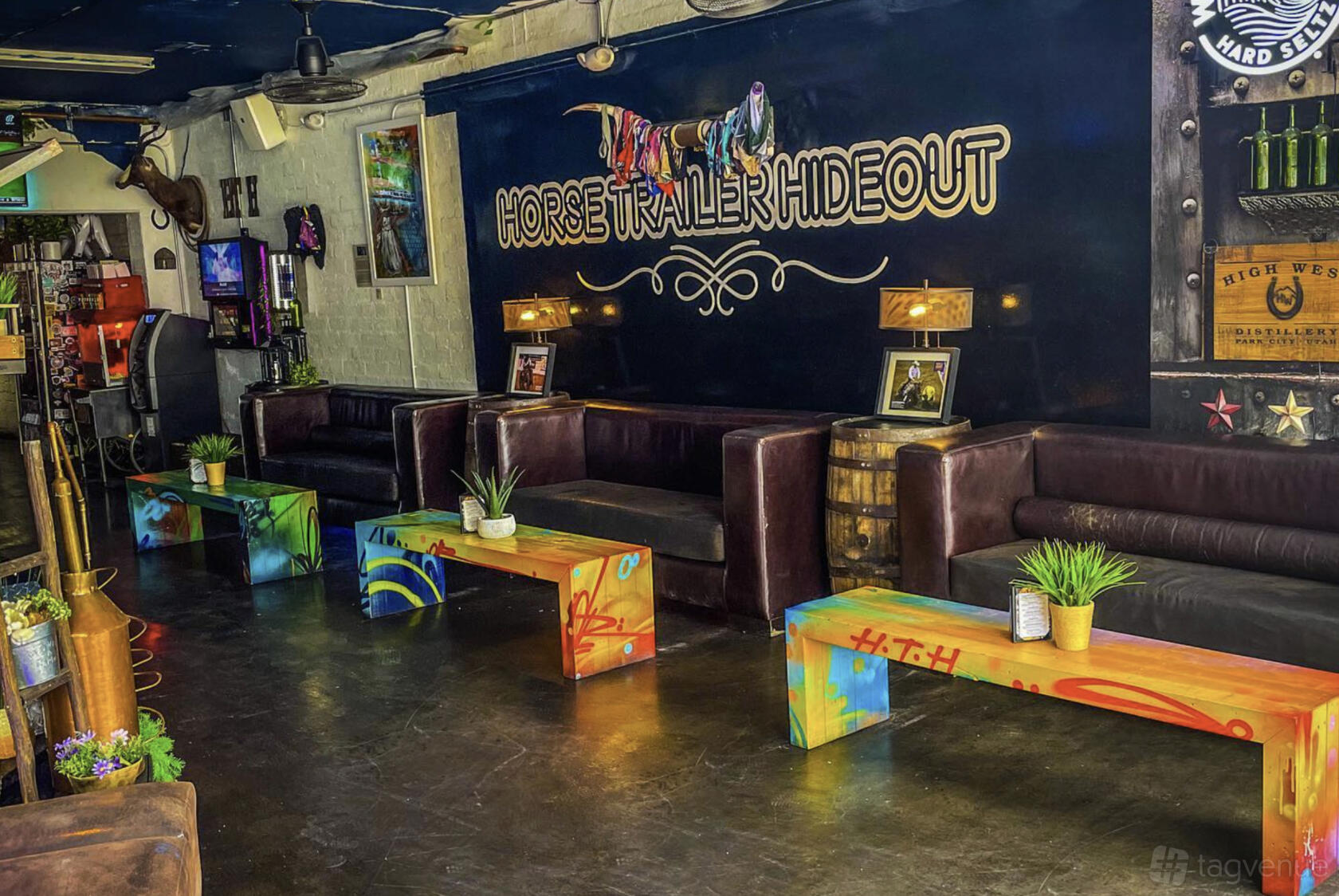 An event space with graffiti-style benches, black leather seating, wall-mounted photos, and potted plants at Horse Trailer Hideout.