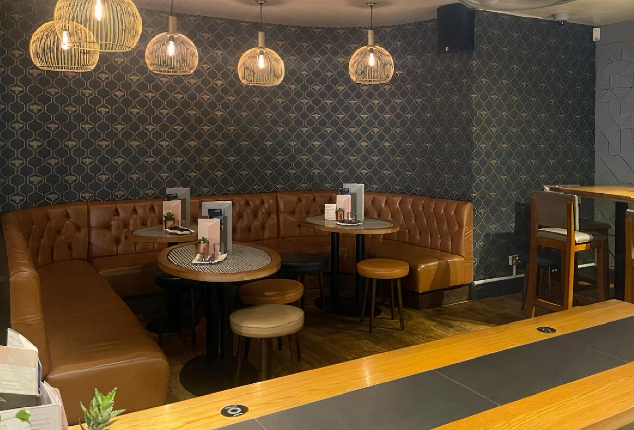 An event space in a bar with tufted leather banquette seating, round tables, and pendant lighting at All Bar One Manchester.