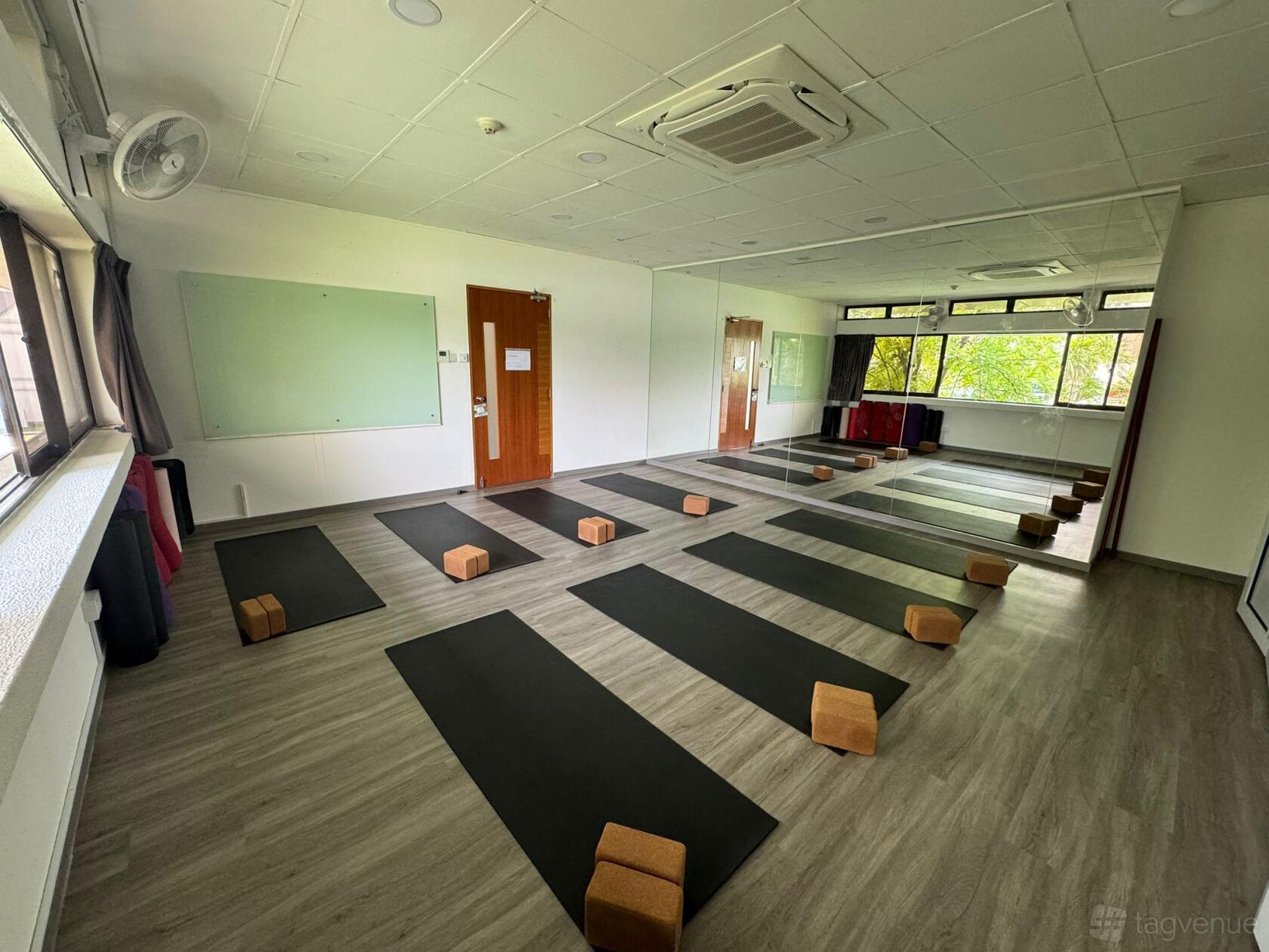 A yoga studio with wood floors, yoga mats and blocks, tall windows, and wall mirrors at Vyasa Yoga Singapore.