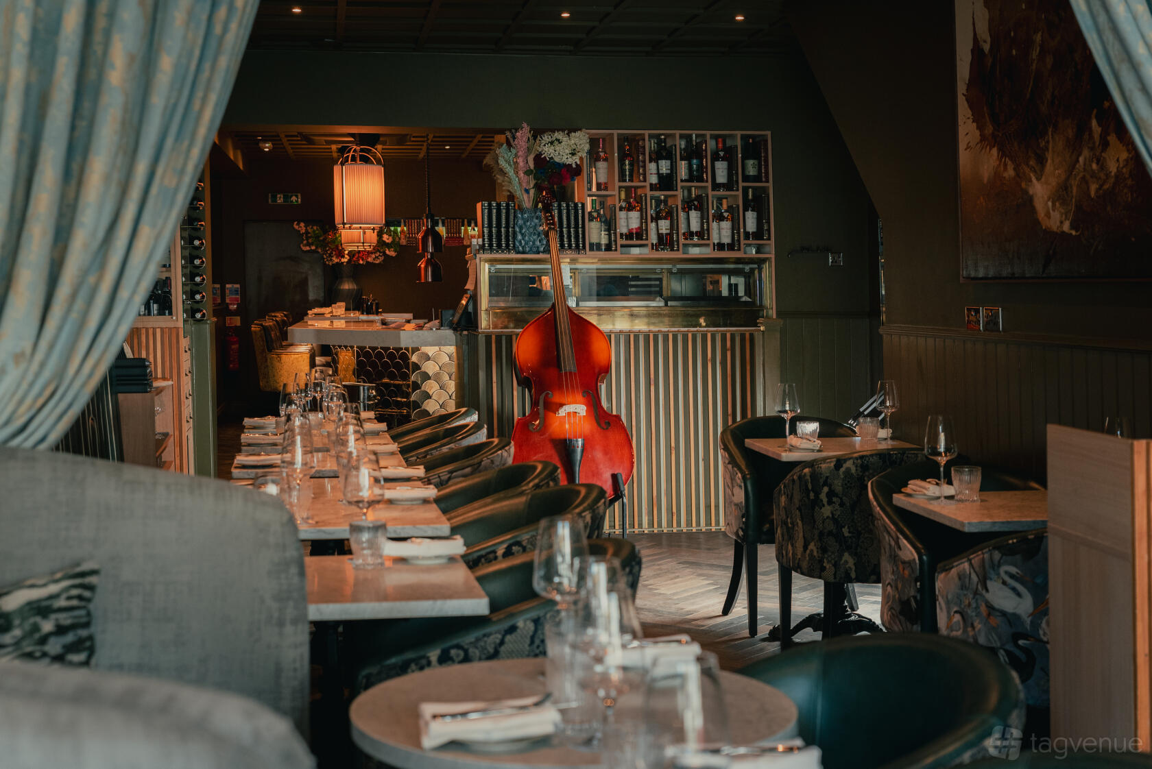 A restaurant dining area with marble-topped tables, upholstered chairs, and a double bass displayed by the wine racks at La Bibliotheque.