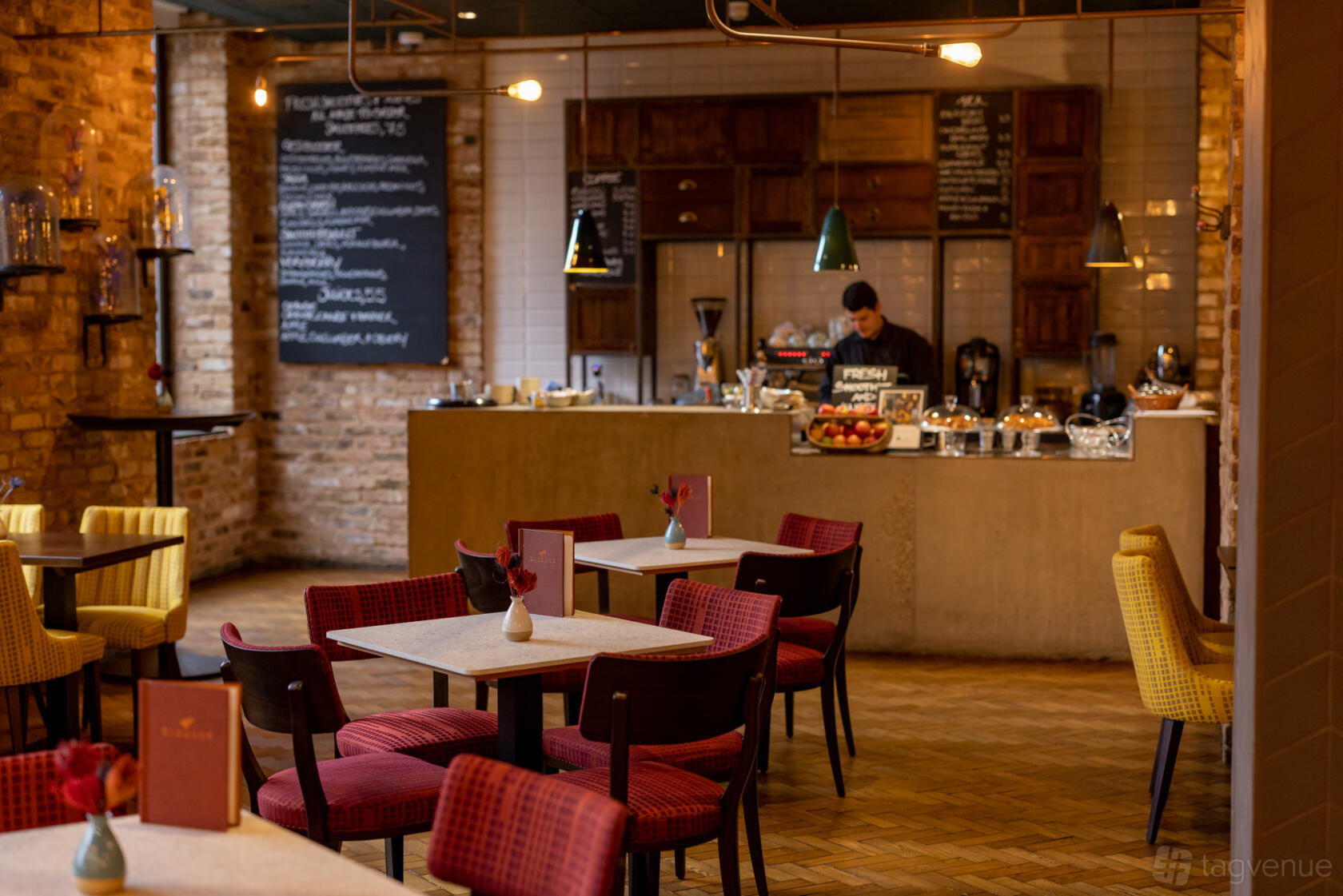 A bar in a pub with exposed brick walls, chalkboard menus, and colorful upholstered chairs at Broadwood.