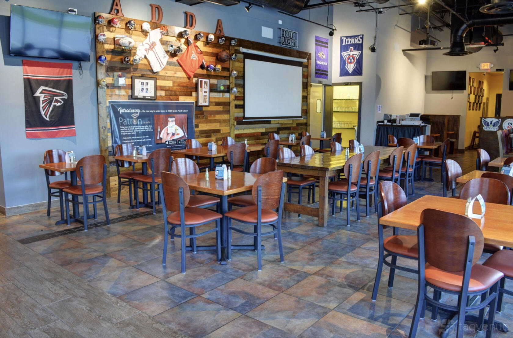 An event space with wooden tables, sports memorabilia on the walls, and flat-screen TVs at Adda Sports Pub & Bar.