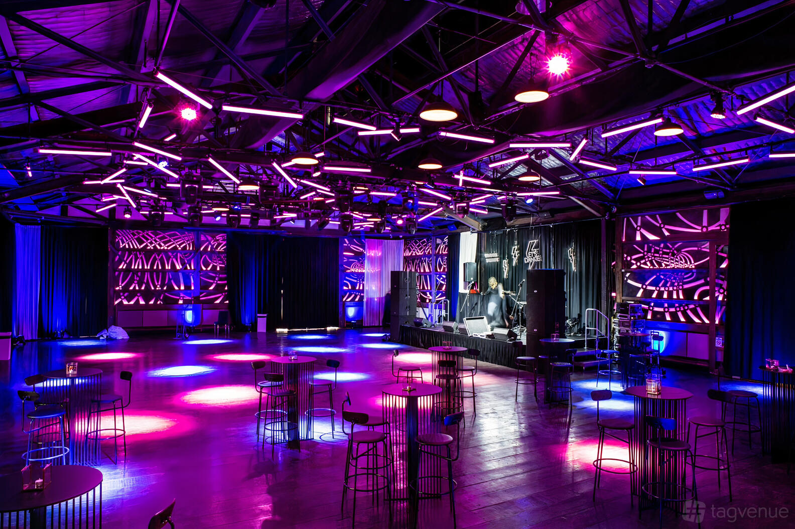 A hall with dramatic purple lighting, exposed ceiling beams, and scattered cocktail tables at Showtime Events Centre.