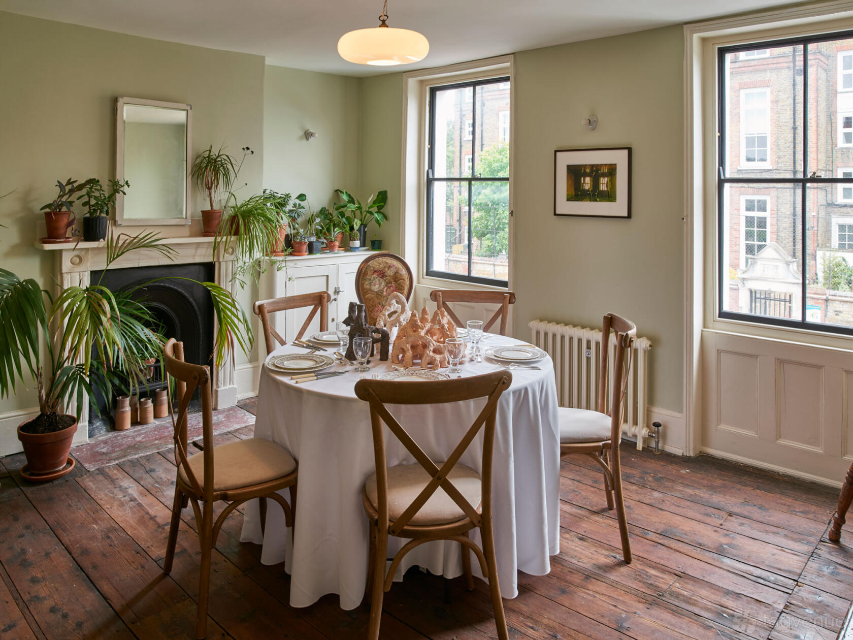 An event venue with large sash windows, wooden floors, and a round dining table with place settings at Van Gogh House.
