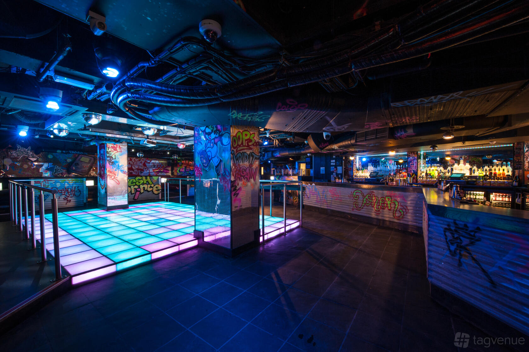 An event space in a nightclub with a glowing LED dance floor, graffiti walls, and colorful lighting at LUXE.