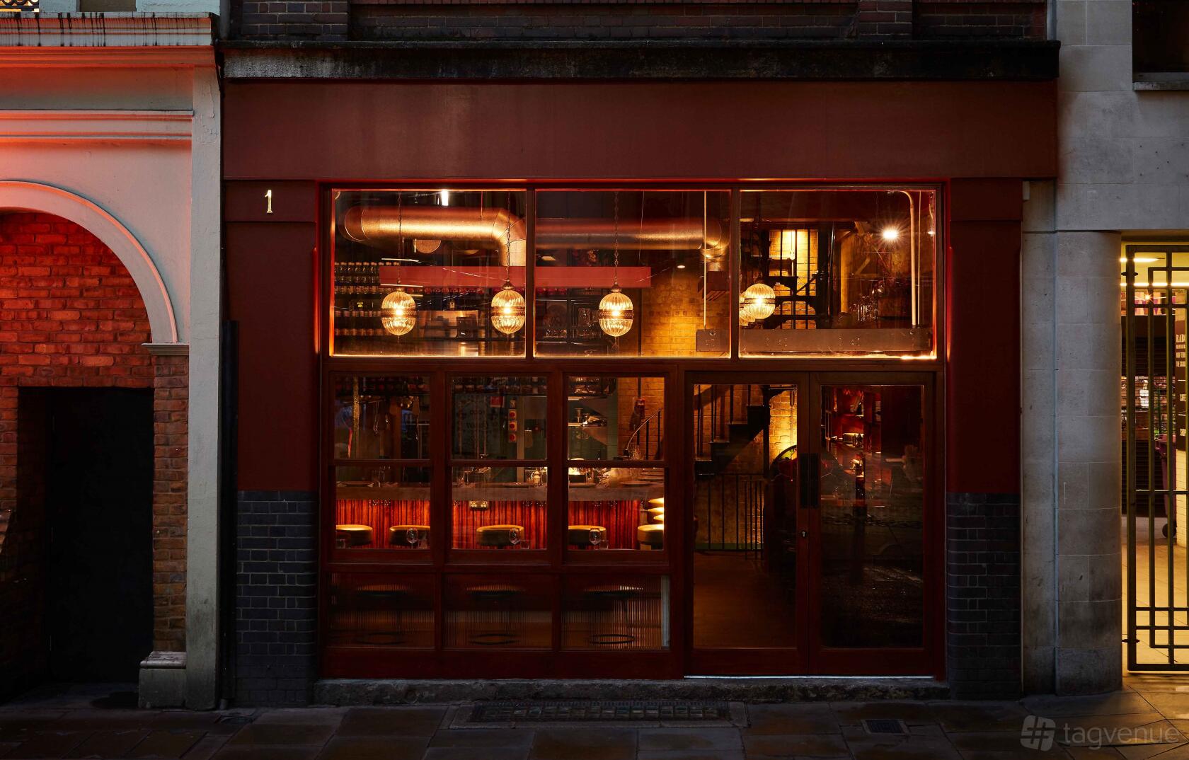 A restaurant with large glass windows, red frames, and warm pendant lighting at Berenjak Borough.