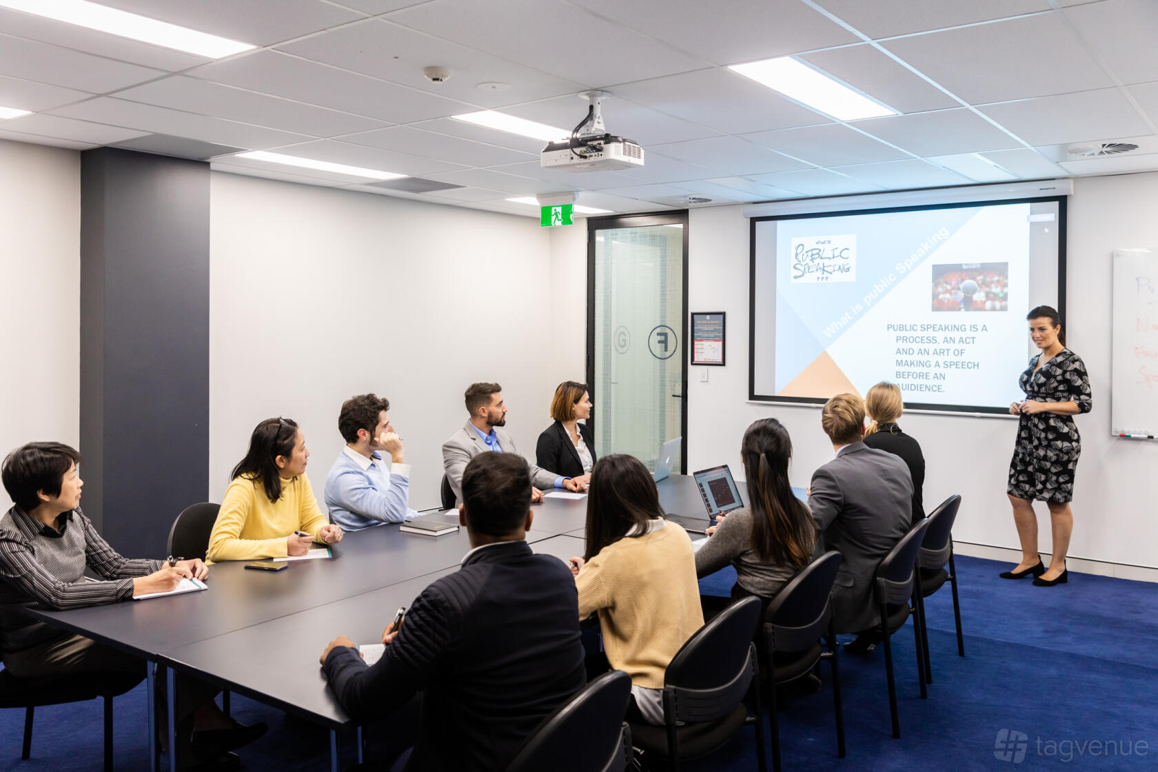 A conference centre with a rectangular table, office chairs, projection screen, and glass walls at Christie Spaces Conferencing Sydney.