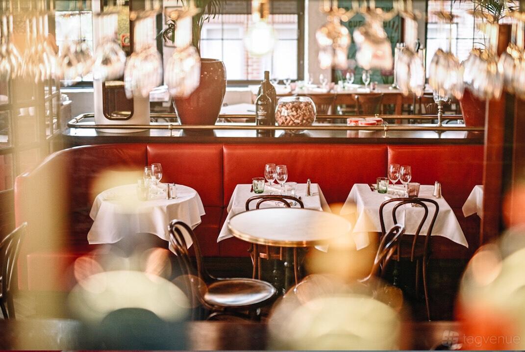 A restaurant with red leather banquette seating, round tables with white linens, and wine glasses at Gavroche Chippendale.