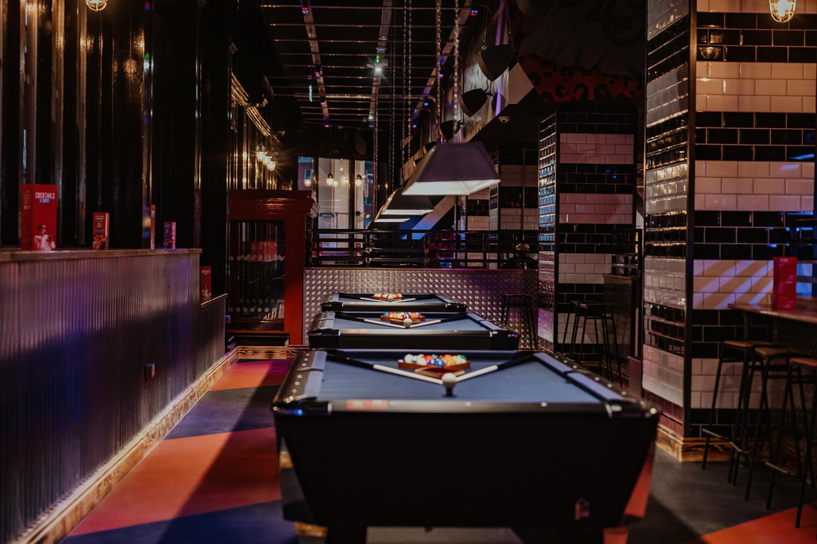 An event space in a bar with a row of pool tables, pendant lighting, and black-and-white tiled walls at Roxy Ball Room Victoria Square.
