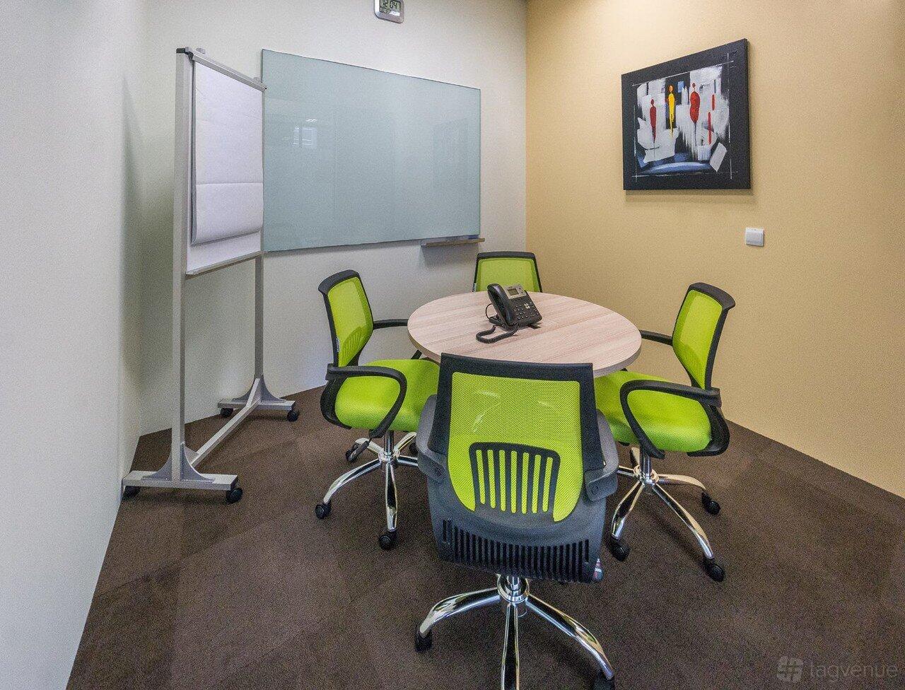 A meeting room with a round table, green chairs, a whiteboard, and a flip chart at Tokio Marine Centre.