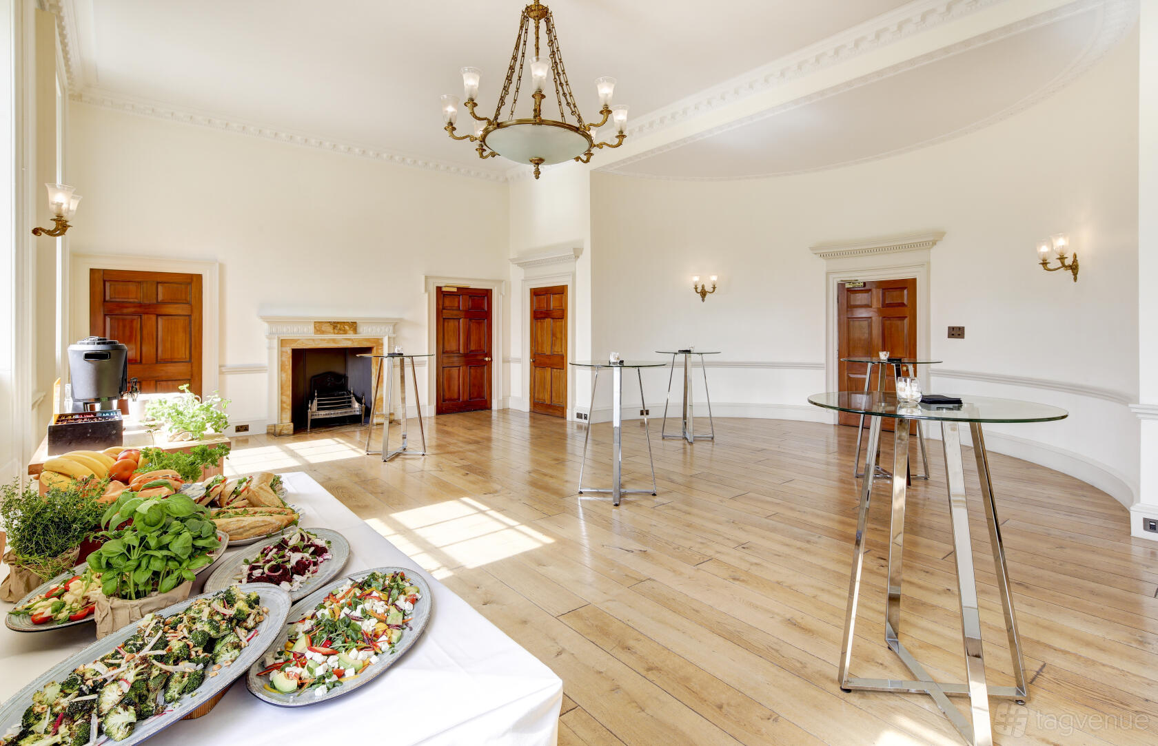 An event venue with high ceilings, a chandelier, wooden floors, and buffet tables set up in the Navy Board Rooms at Somerset House.