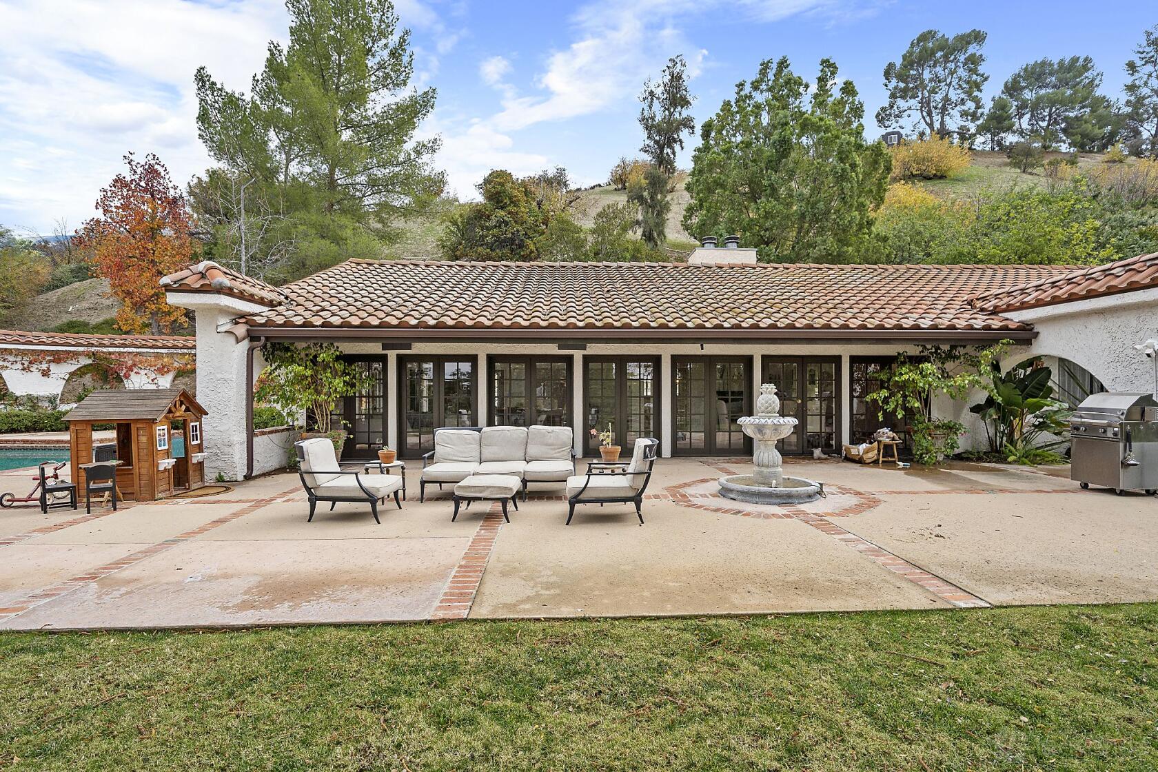 A house with a tiled roof, outdoor patio seating, a stone fountain, and a view of mature trees at Casa Berliner.