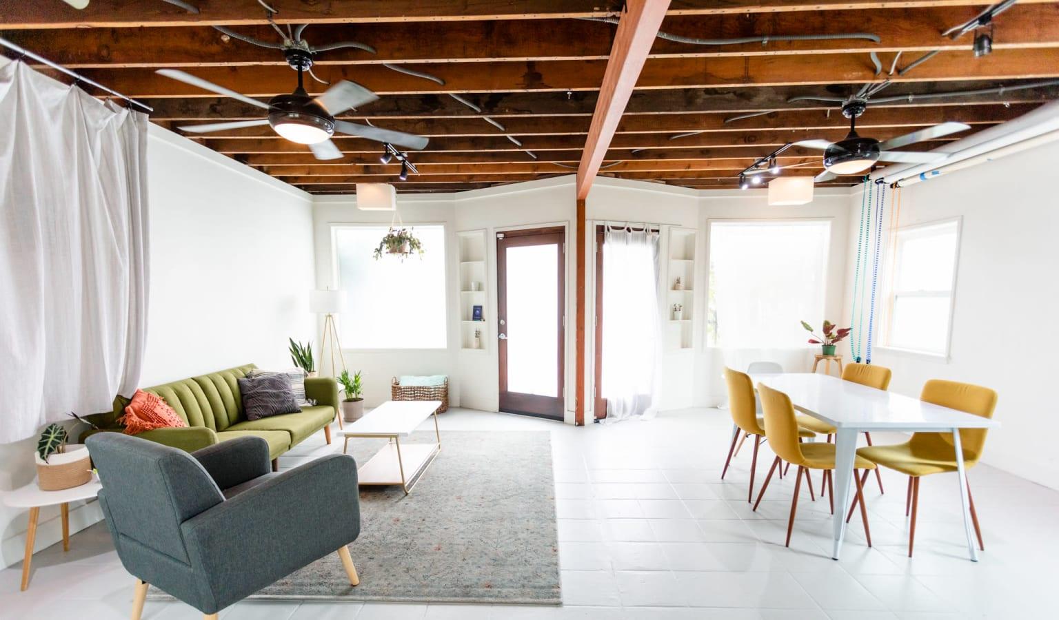 A photo studio with exposed wooden ceiling beams, large windows, and a lounge seating area at Indigo Studio LA.