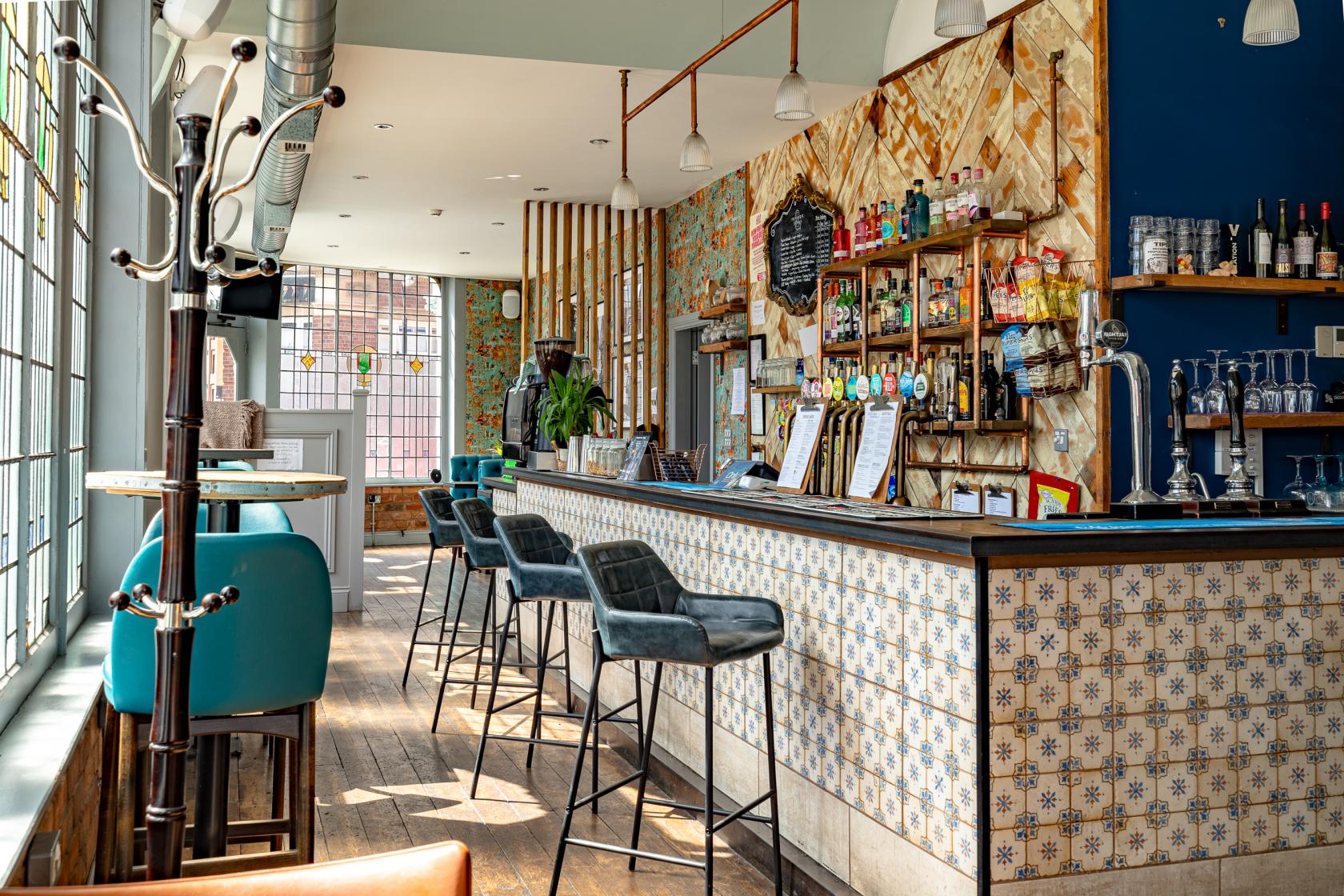 A bar with patterned tile front, high stools, and floor-to-ceiling windows at Temper and Brown.