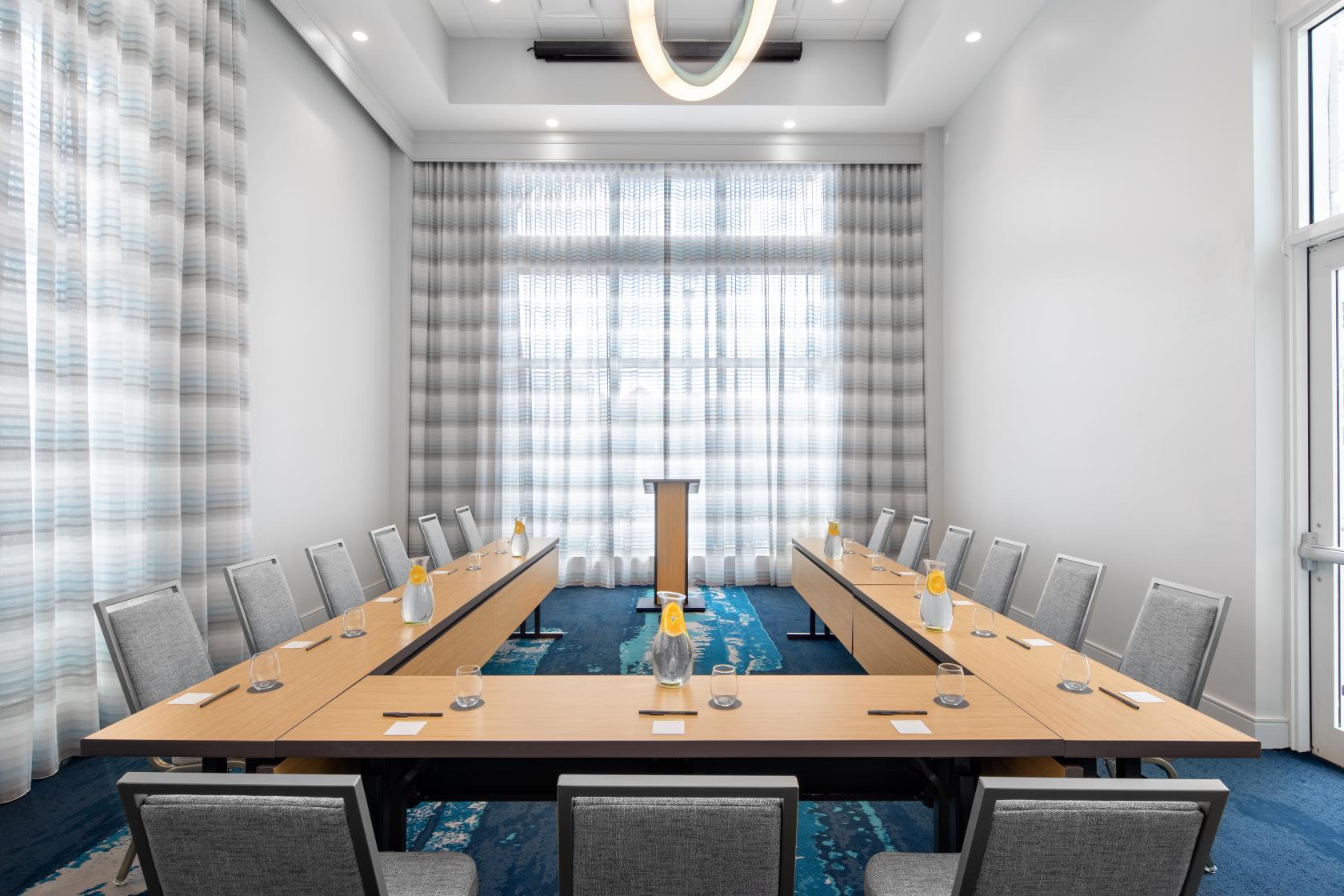 A hotel meeting room with a U-shaped conference table, bottled water, notepads, and floor-to-ceiling windows at Courtyard Delray Beach.