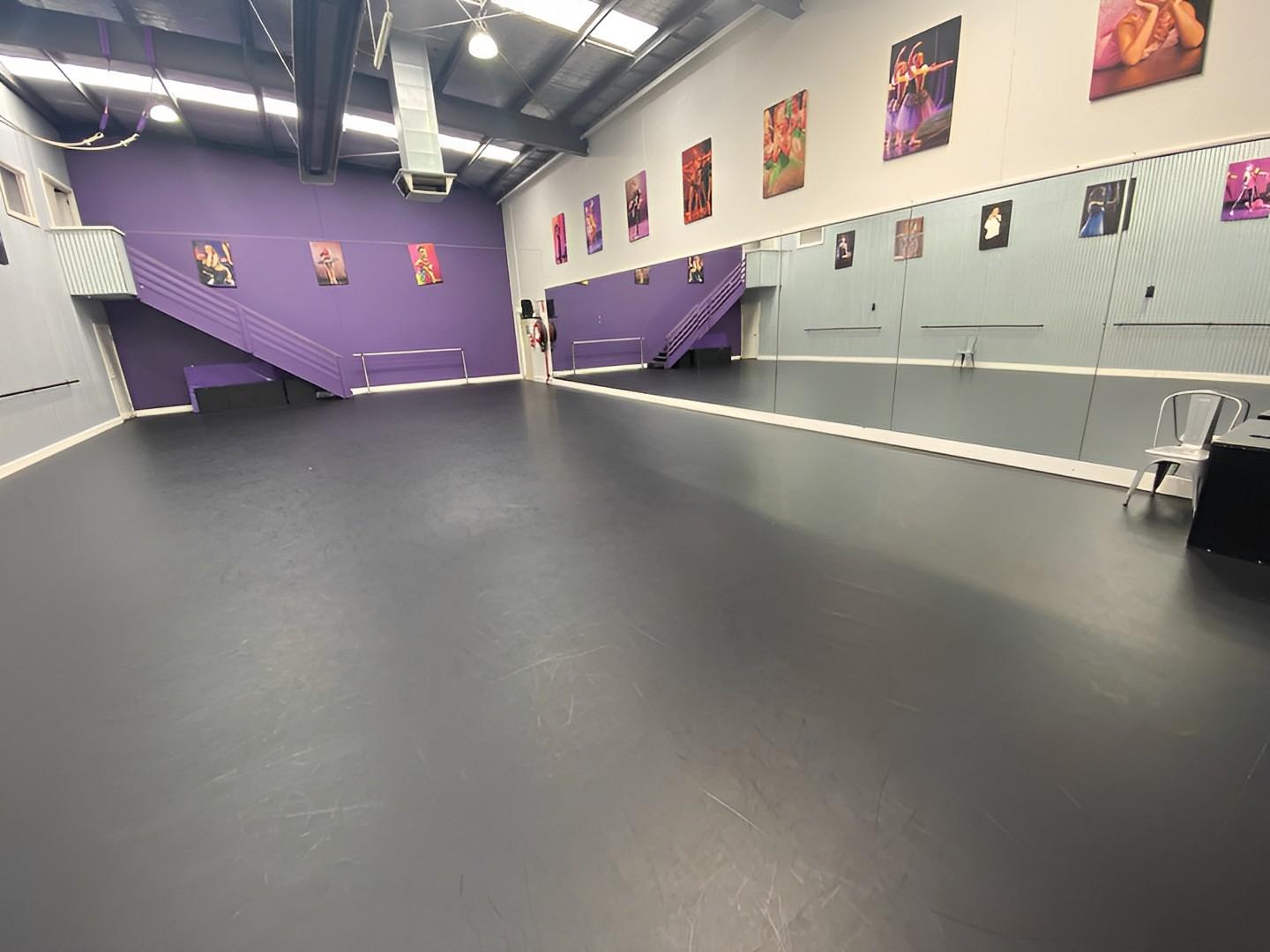 A rehearsal room with a black sprung dance floor, floor-to-ceiling mirrors, and purple accent walls at The Edge Performers School.