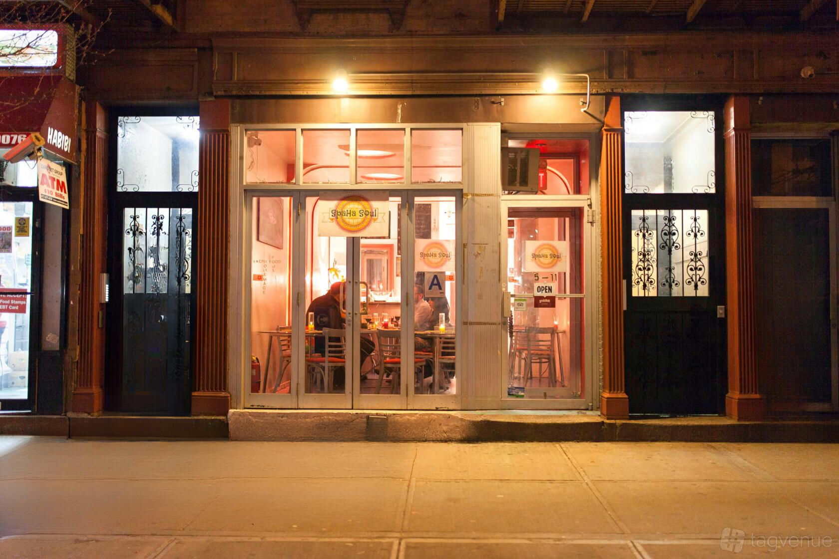 A restaurant with floor-to-ceiling windows, warmly lit interior, and visible dining tables at Spaha Soul.