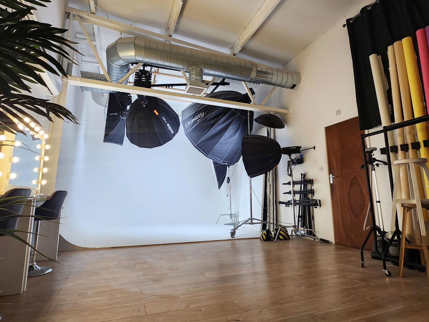 A photo studio with a white infinity cove, studio lighting equipment, and wooden flooring at QUEST Studios London.