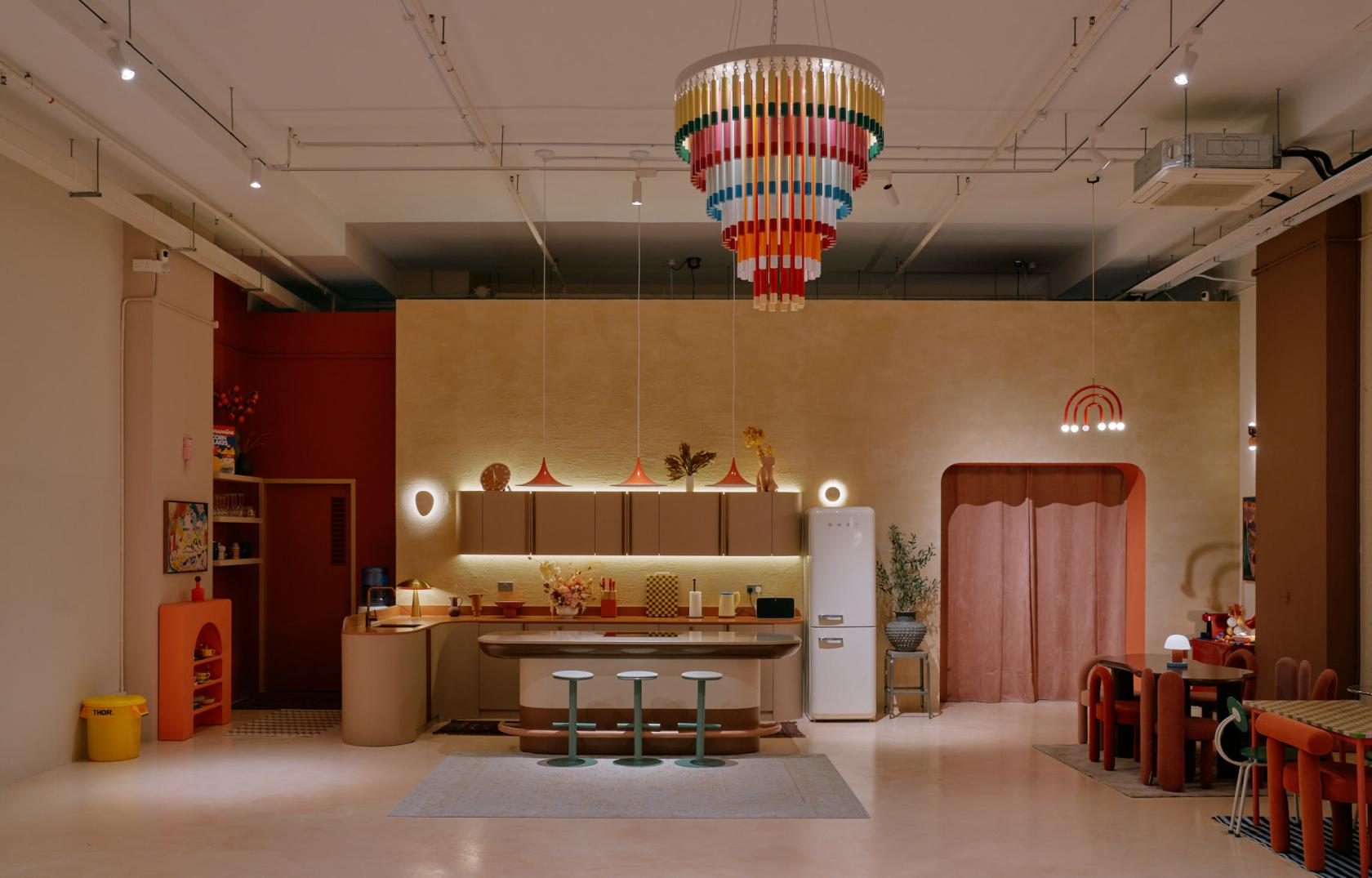 A photo studio with colorful hanging chandelier, open kitchenette, and pastel stools at Studio Min Max.