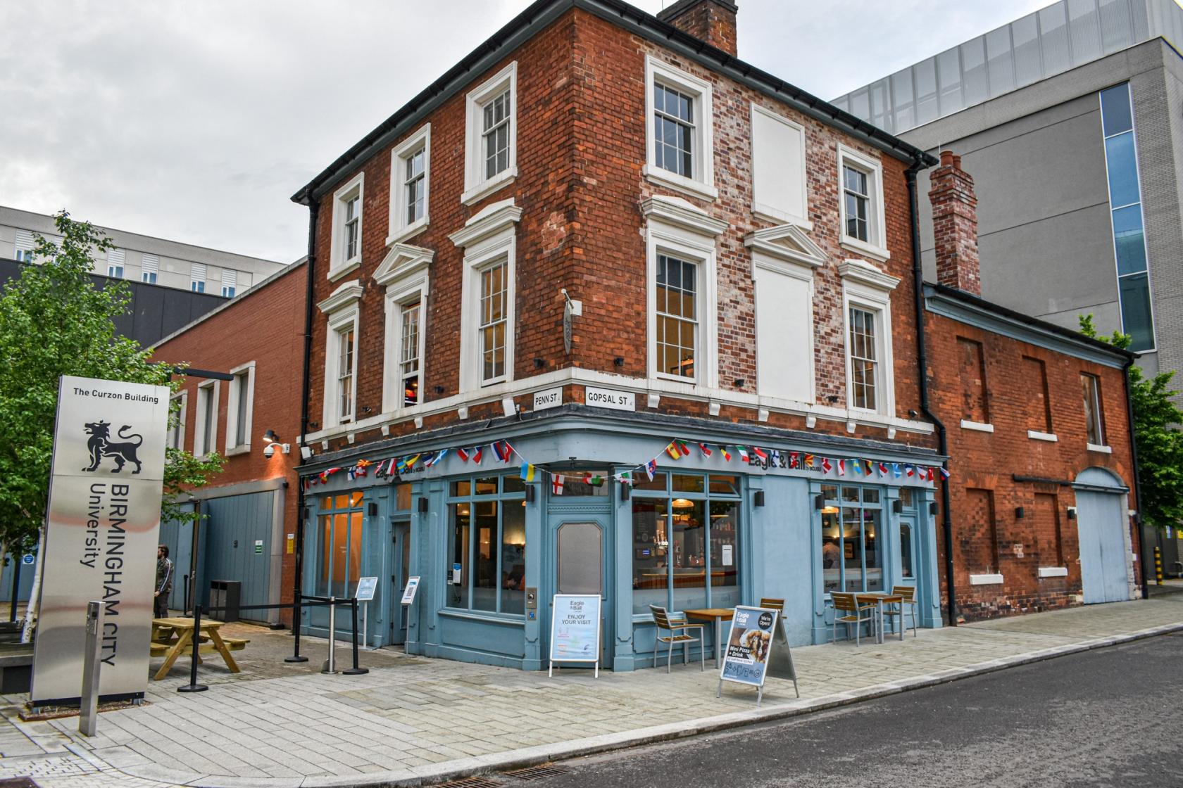 A brick pub with large windows, outdoor seating, and string flags above the entrance at Eagle & Ball.