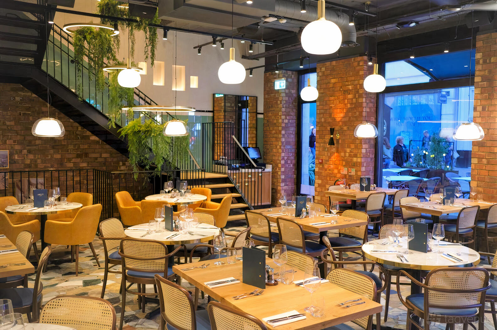 A restaurant with exposed brick walls, pendant lighting, rattan chairs, and a staircase with greenery at Amalfi Ristorante.
