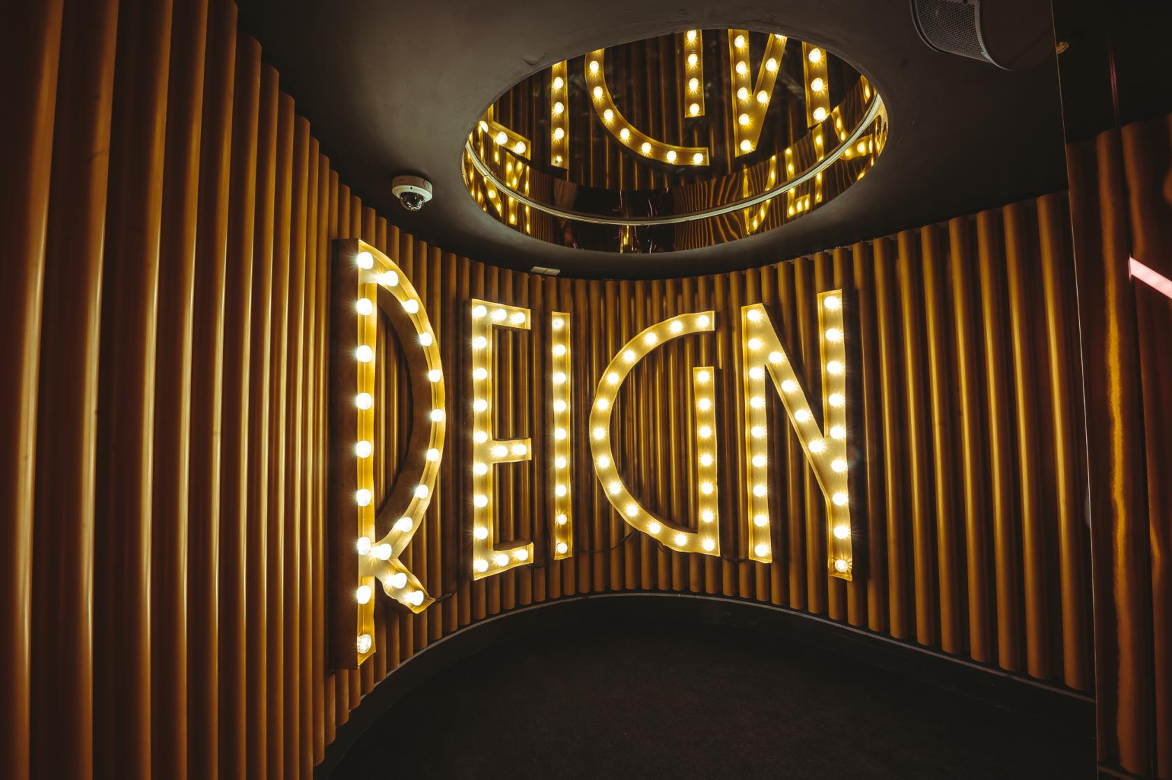 A nightclub entrance with illuminated REIGN letters on curved gold wall panels at The London Reign - Strongarm Hospitality.