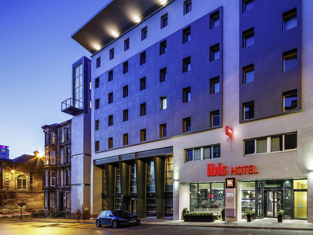 A hotel exterior with large windows, modern facade, and illuminated entrance at Ibis City Centre.