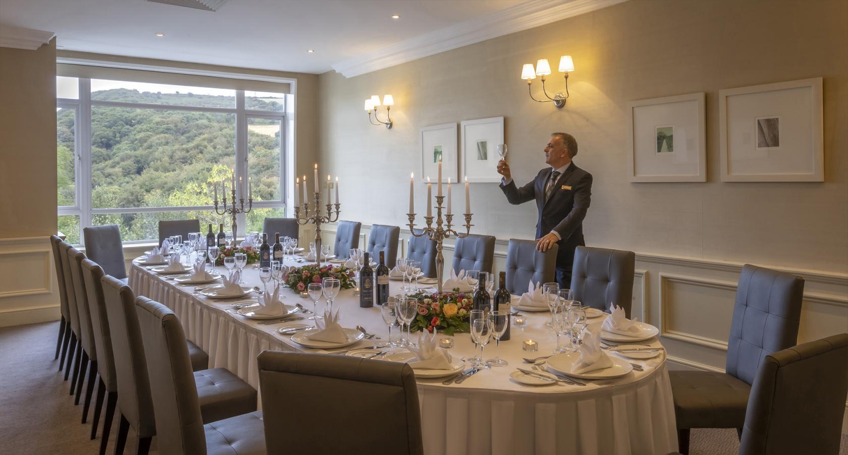 A hotel boardroom with a long oval table set with white linens, floral centerpieces, and candelabras at Glenview Hotel & Leisure Club.
