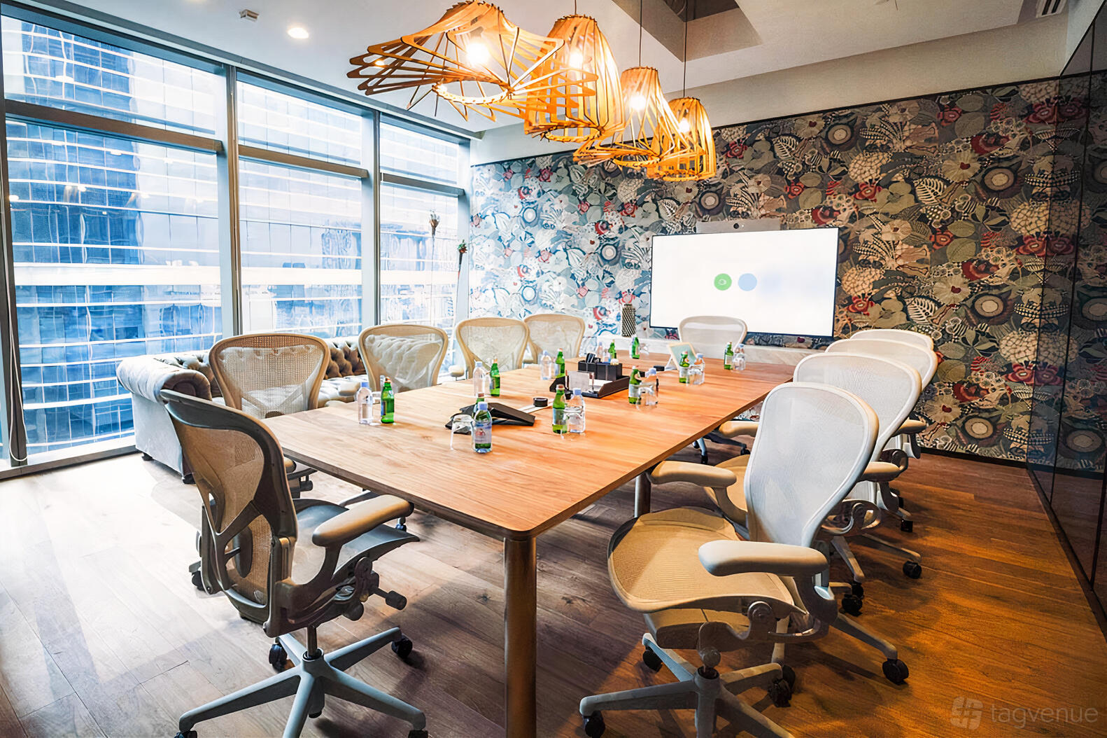 A coworking space with a long wooden table, ergonomic chairs, floor-to-ceiling windows, and pendant lights at Frasers Tower.