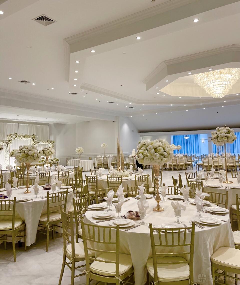 A ballroom with gold chiavari chairs, round tables with white linens, and tall floral centerpieces at Riverview Ballroom.
