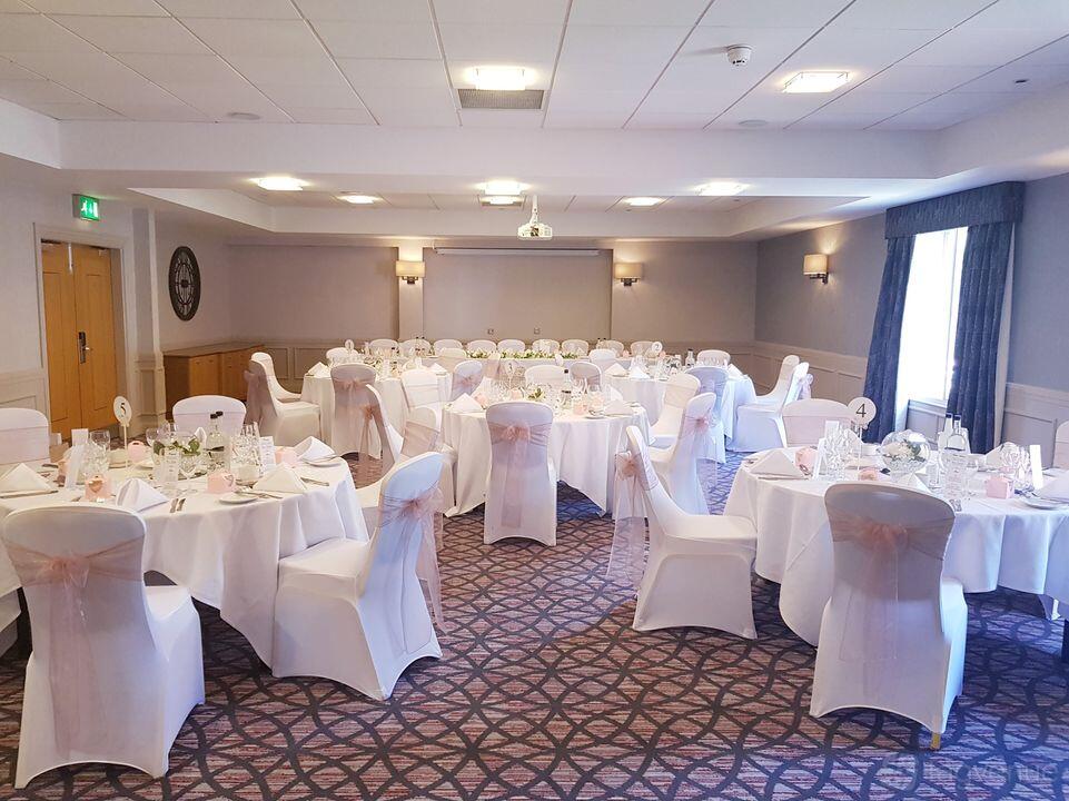An event space in a hotel with round tables set with white linens and chair covers at Chesford Grange.