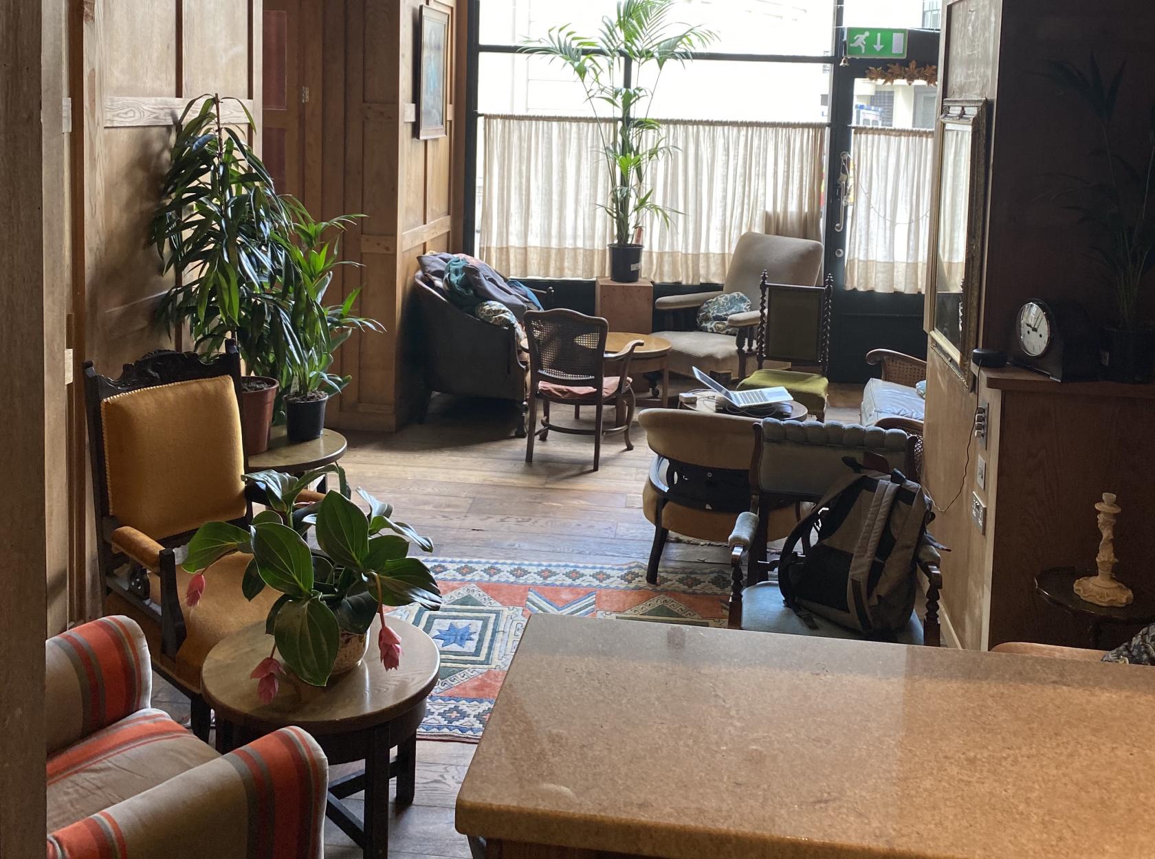 A lounge with upholstered armchairs, potted plants, and natural light from tall windows at Brydges Place Club.