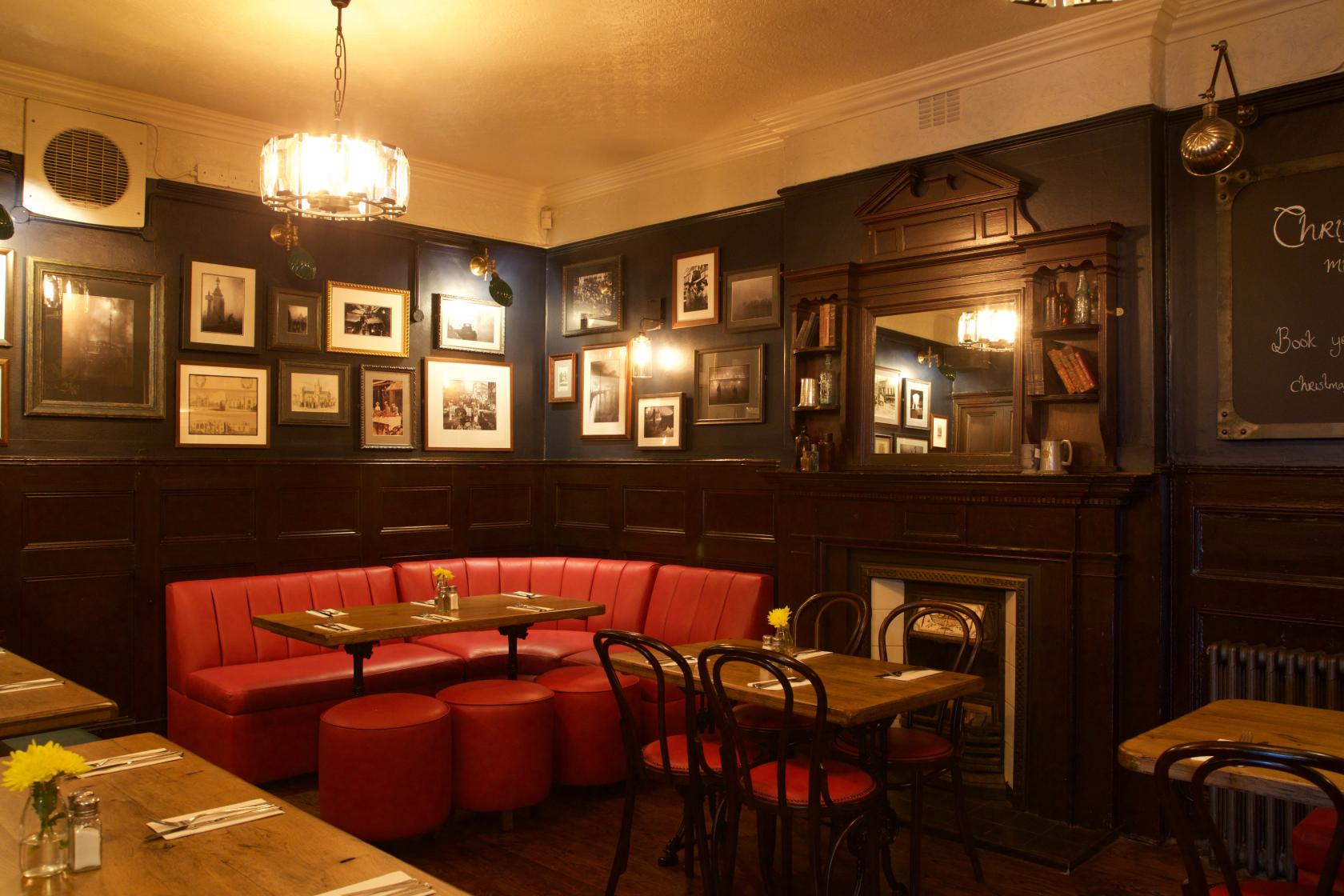 An event space in a pub with red banquette seating, framed photos, dark wood paneling, and a fireplace at The Crown Tavern.