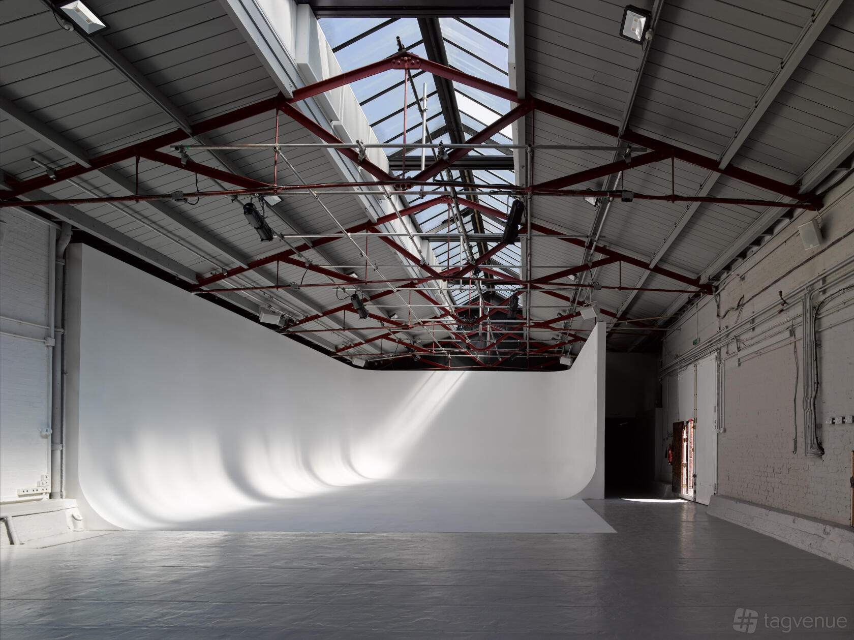 A photo studio with a large white cyclorama wall, high ceilings, and overhead skylights at Park Village Studios.
