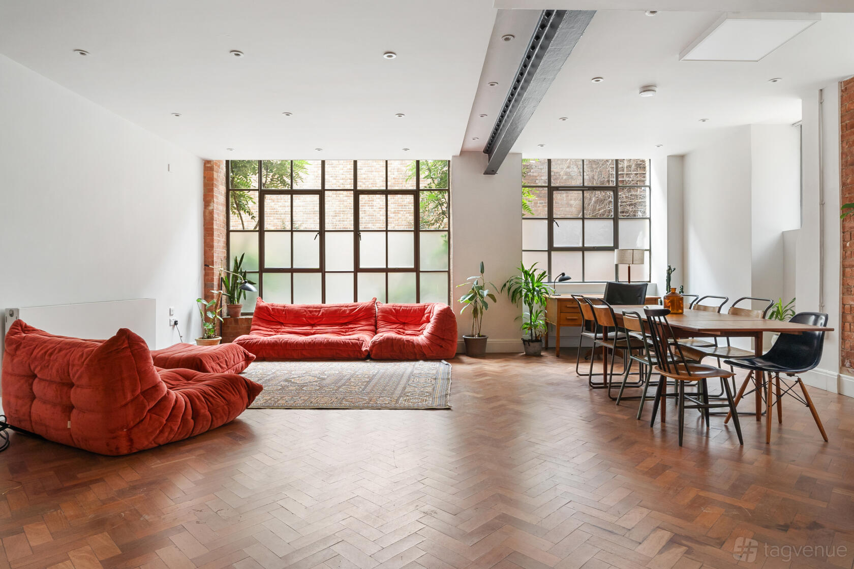 A creative space with large factory windows, red sectional sofas, parquet floors, and greenery at Chocolate Studios.