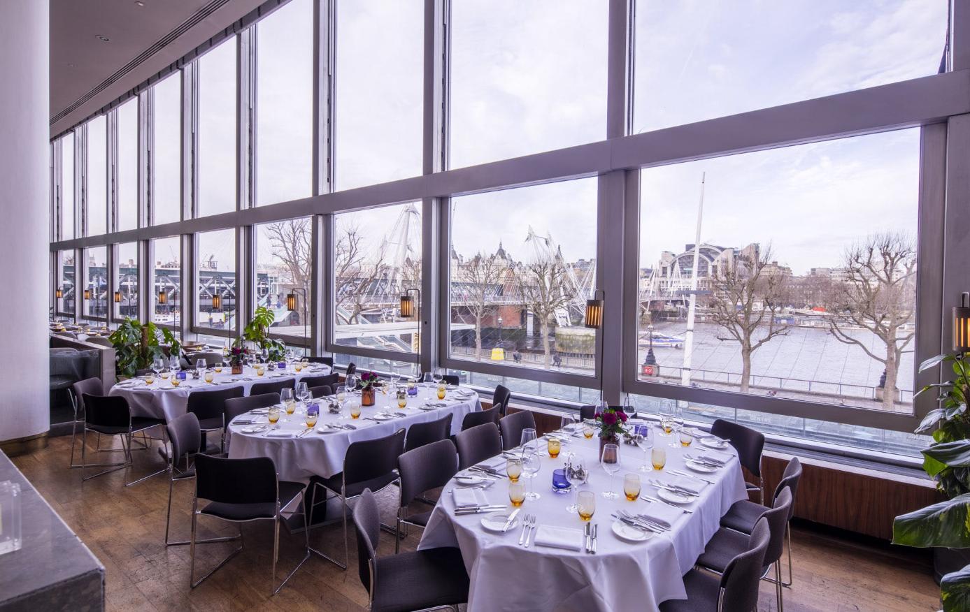 A restaurant with floor-to-ceiling windows, round tables with white linens, and river views at Skylon.
