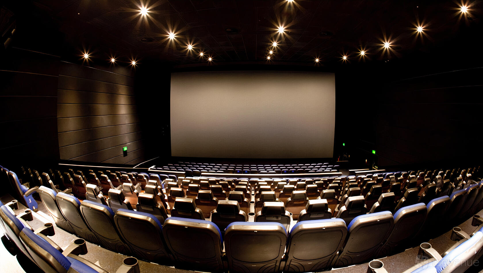 A cinema screening room with tiered seating, wide blank screen, and spotlight ceiling lights at ODEON Trafford Centre.