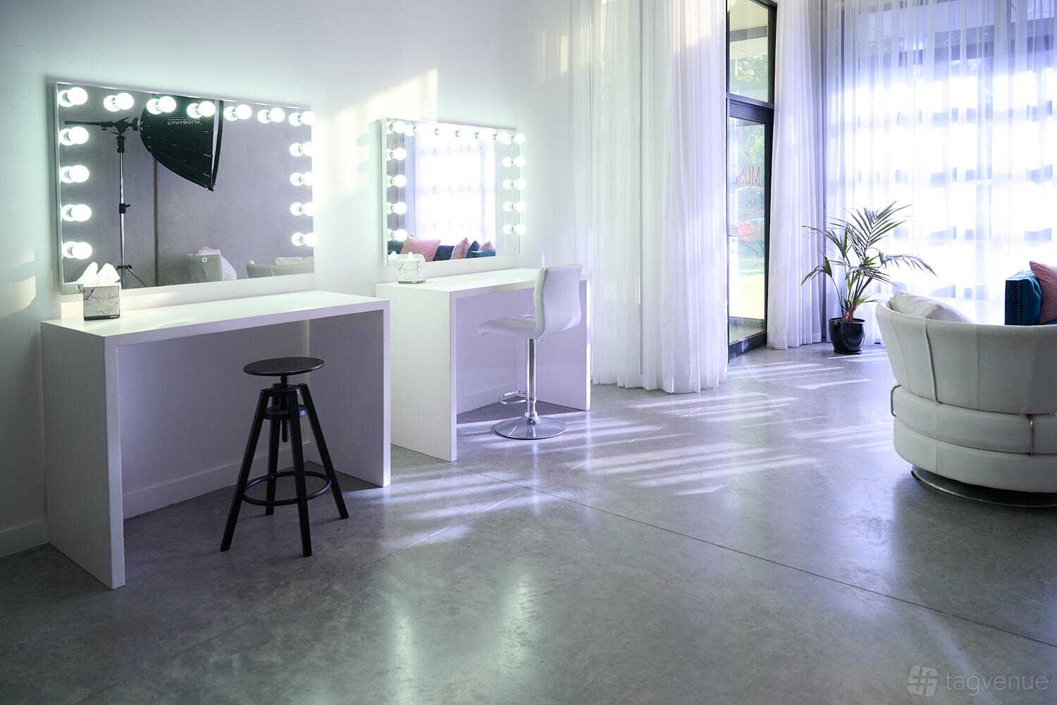 A photo studio with illuminated makeup stations, sheer curtains, and a white lounge chair at Muse Studio.
