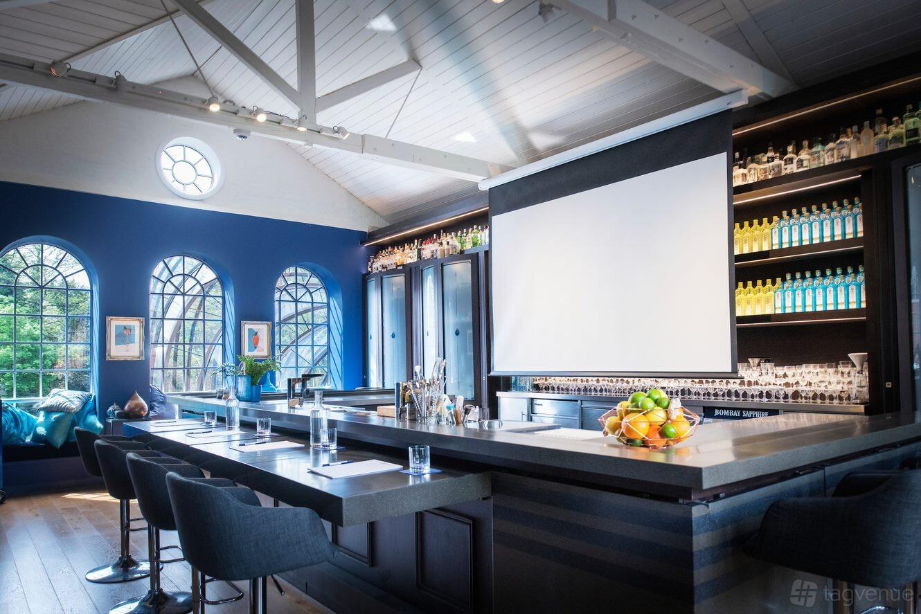 A function room in a winery with high ceilings, arched windows, a stocked bar, and a projector screen at Bombay Sapphire Distillery.