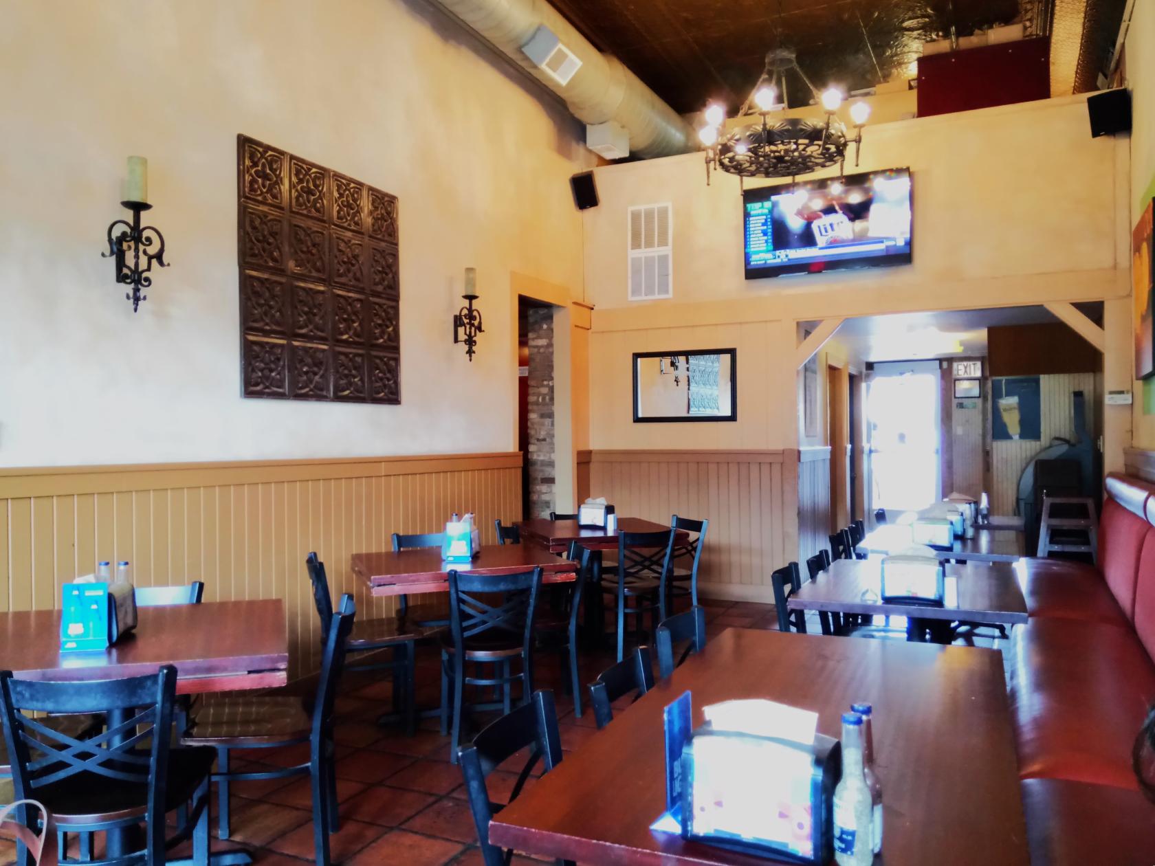 A dining room with wooden tables, black chairs, wall sconces, and a mounted TV at Potter's Place and Two-Nine Martini Lounge.