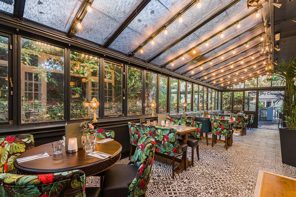 A pub with a glass-enclosed dining area, patterned tile floor, and floral upholstered chairs at The Alwyne Castle.