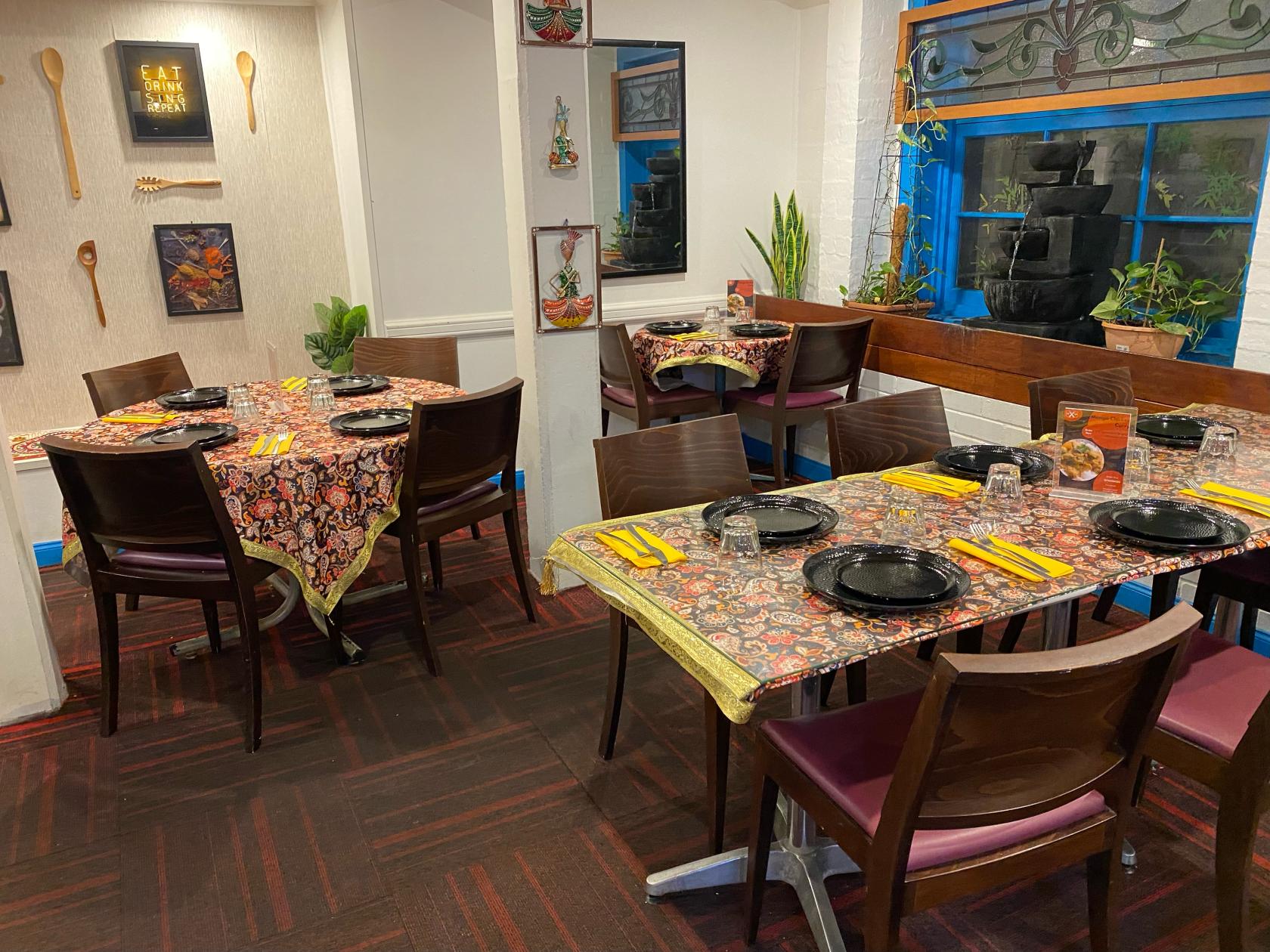 An event space in a restaurant with patterned tablecloths, dark wooden chairs, and wall art at JK Restaurant Tandoori and Curry House.