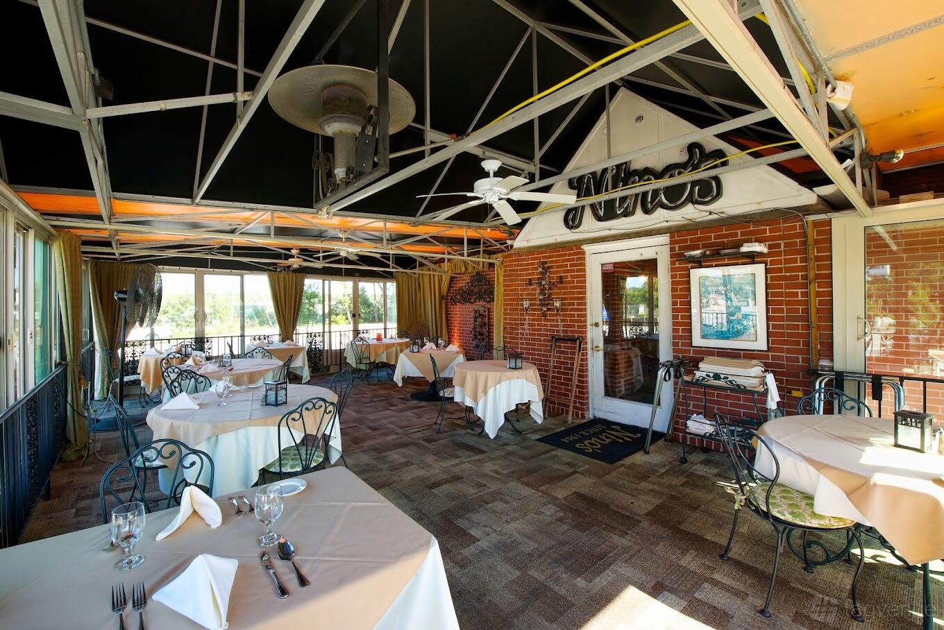 An outdoor dining area with wrought iron chairs, round tables with white linens, and exposed brick walls at Nino's Italian Restaurant.