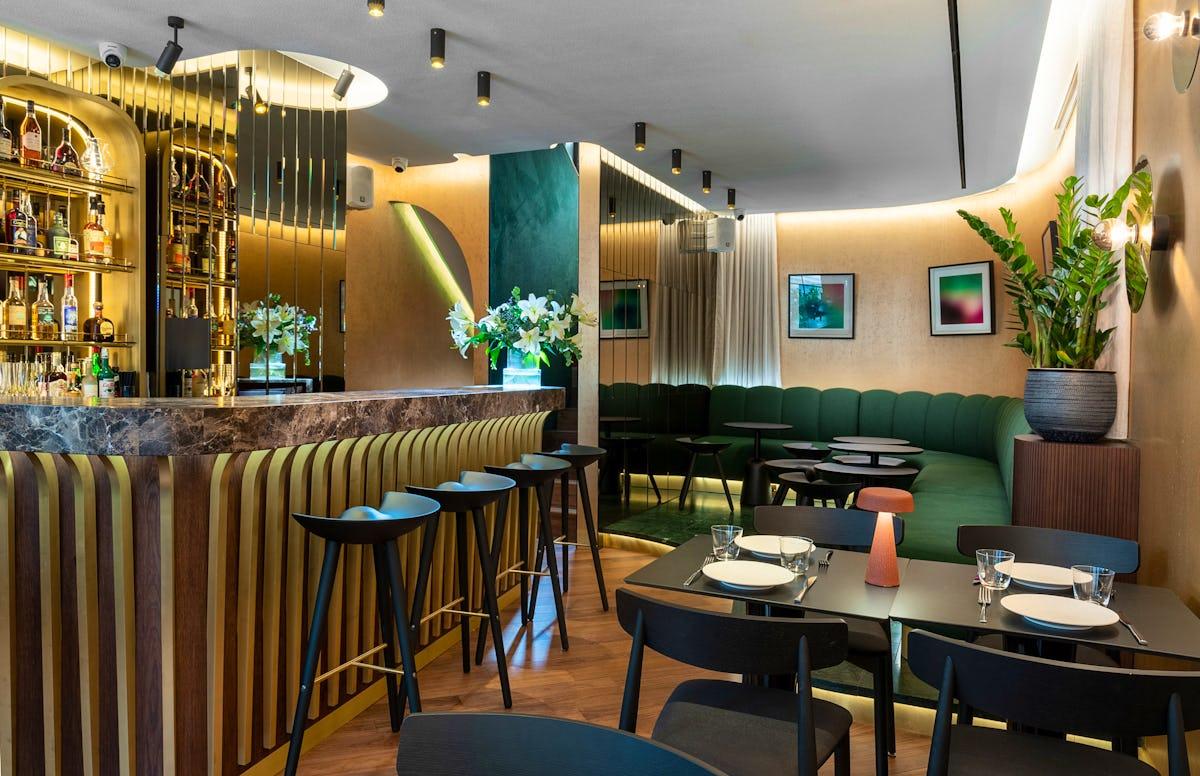 A restaurant with a marble bar, mirrored accents, green velvet banquette seating, and modern decor at Bantof.
