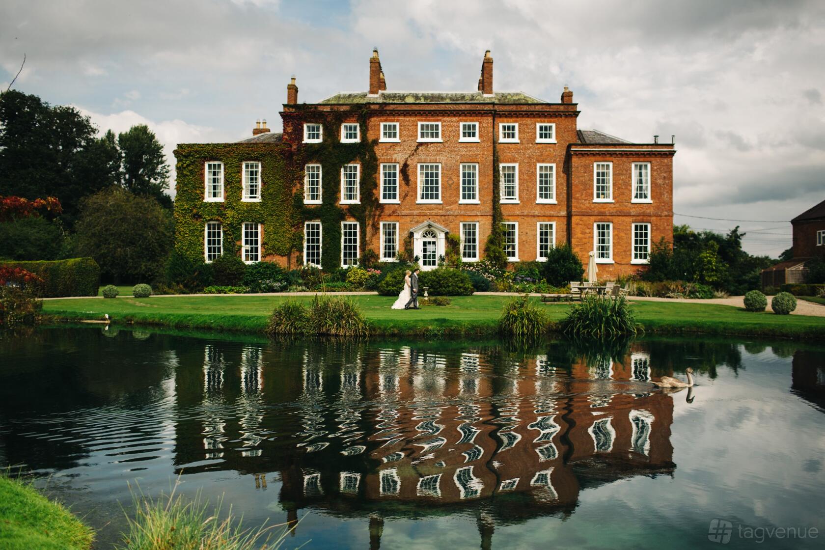 A historic hall with red brick facade, ivy-covered walls, and a landscaped pond at Delbury Hall.
